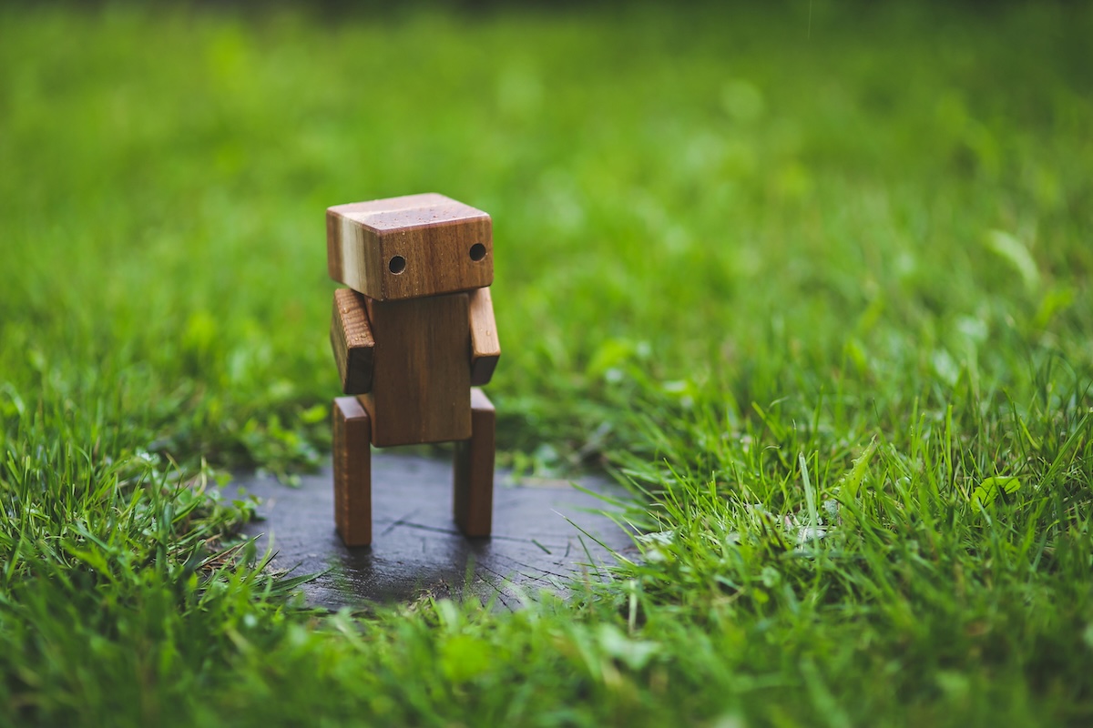 Wooden robot sitting on a rock surrounded by grass